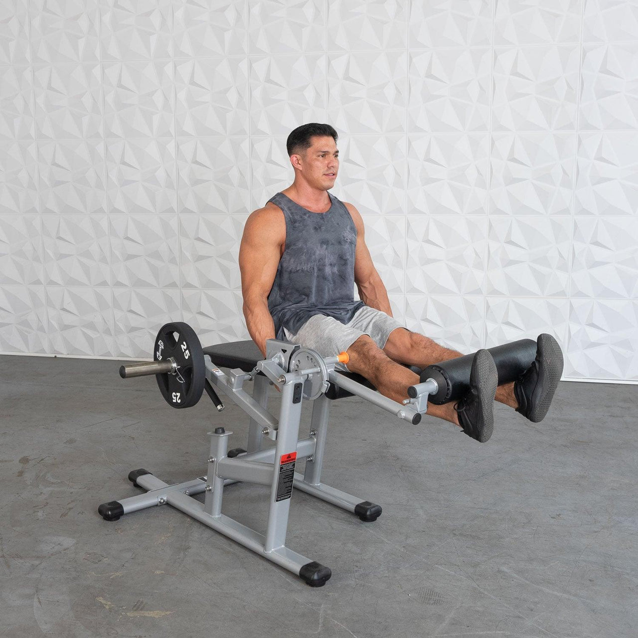 Man using a silver and black plate-loaded leg extension/curl machine with a 25lb weight plate.