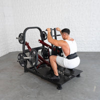 Thumbnail for Man in white tank top and shorts performing a belt squat on a plate-loaded machine.