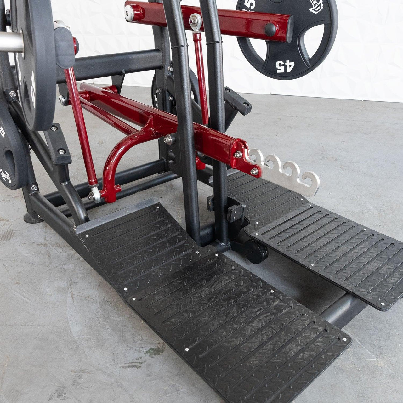 Red and black plate-loaded belt squat machine with textured foot platforms and weight plates.