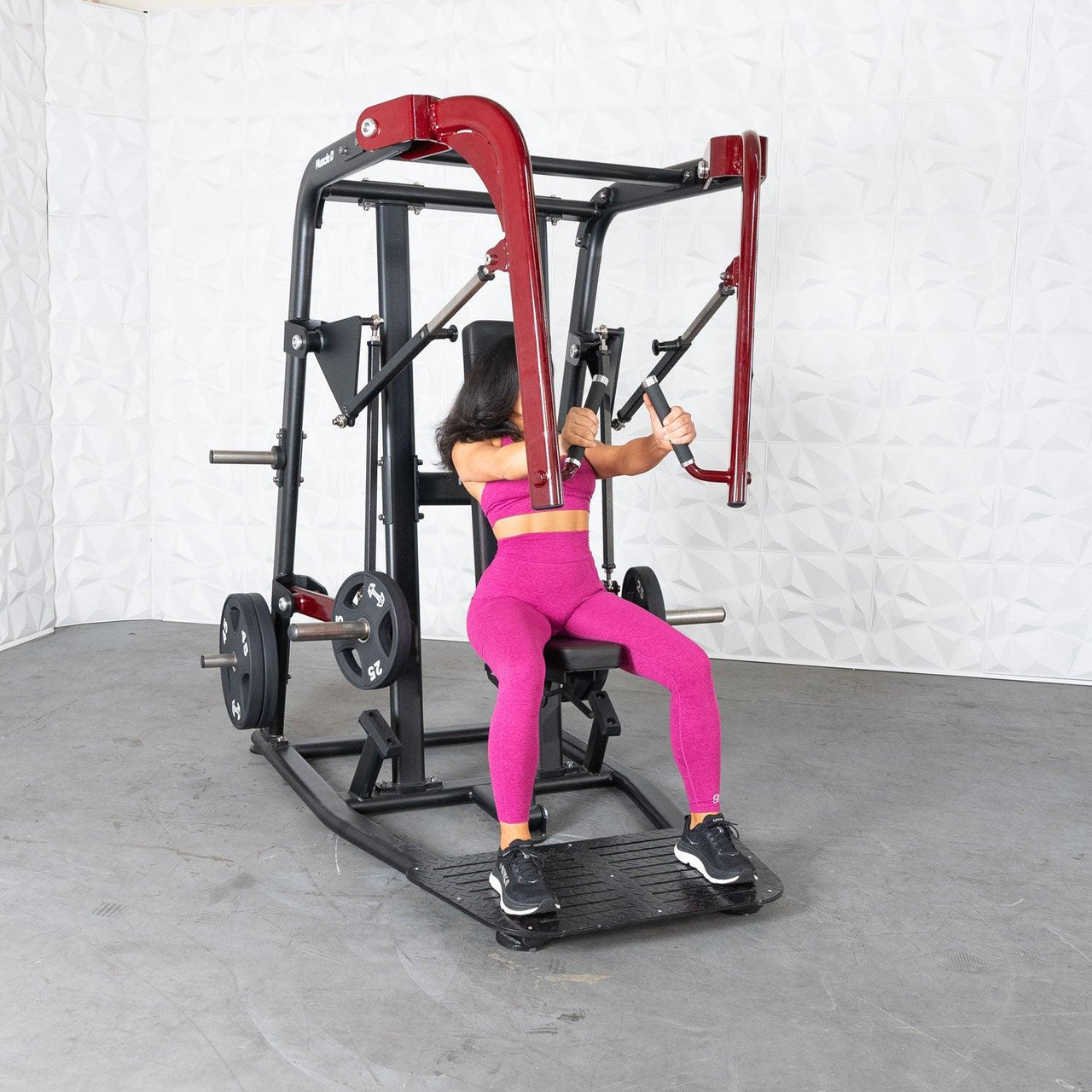 Woman in pink using a black and red plate-loaded chest press machine.