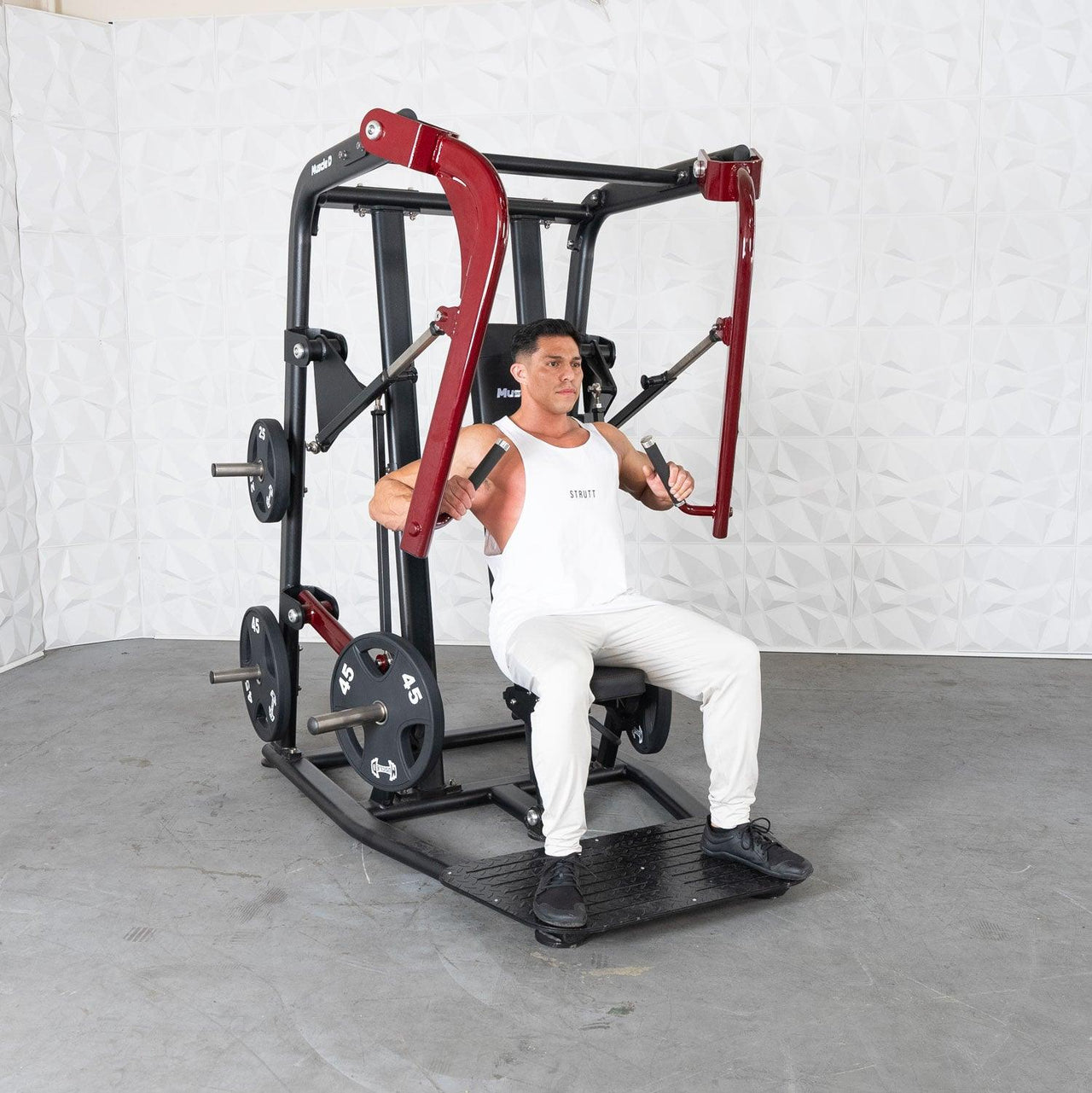 Man in white tank top using a red and black plate-loaded chest press machine.