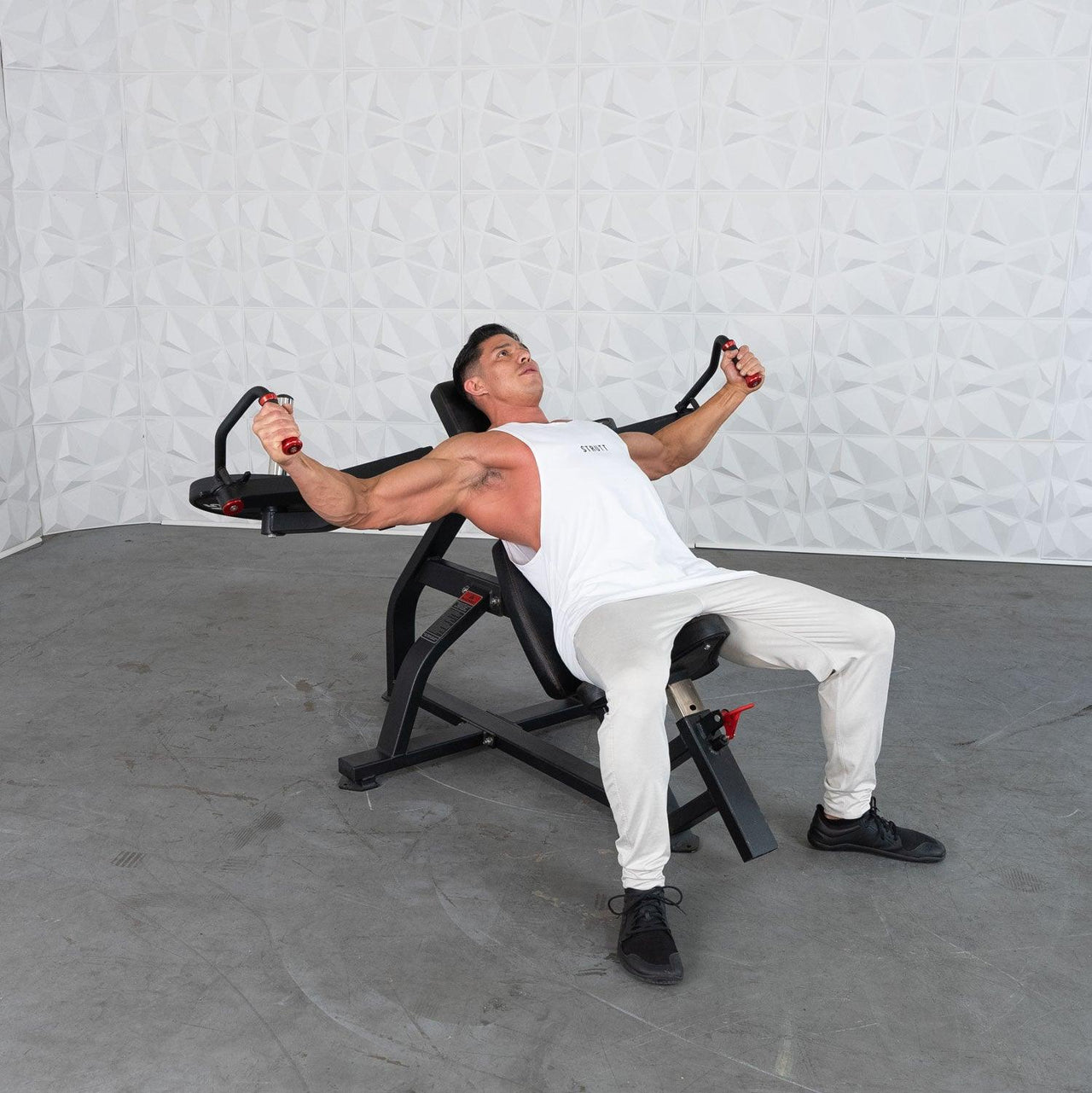 Man in white tank top and light pants using a black incline pec fly machine.
