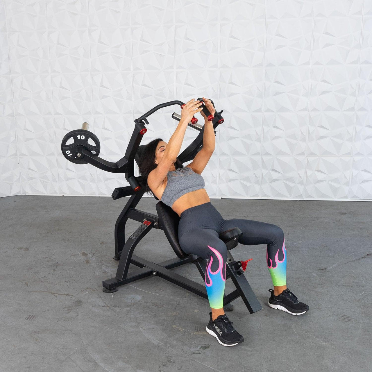 Woman on an incline pec fly machine, pushing handles up, with a 10lb plate loaded.