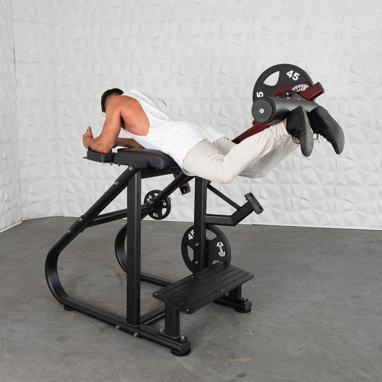 Man using a black plate-loaded reverse hyper machine with a red roller pad, 45lb weight plate attached.