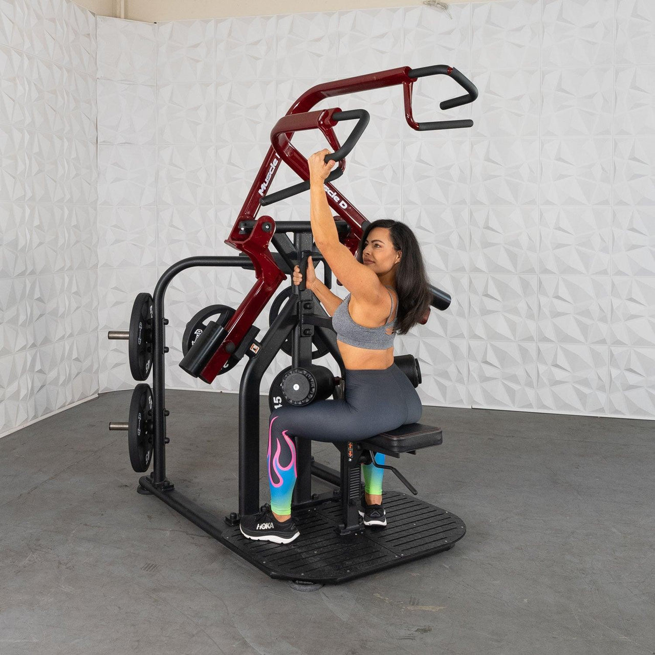 Woman using a red and black rotary lat pull-down machine with plate weights.