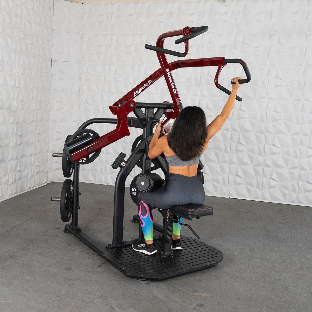 Woman using a red and black plate-loaded rotary lat pull-down machine.