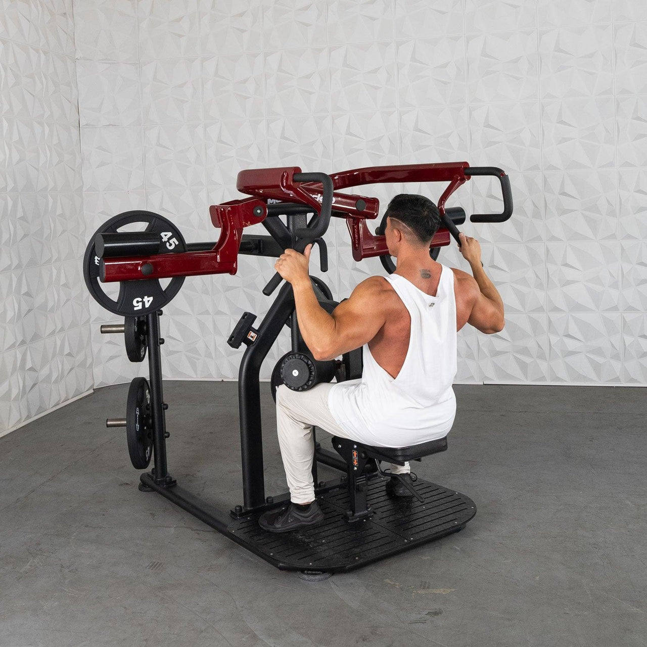 Man in white tank top using a red and black plate-loaded rotary lat pull-down machine.