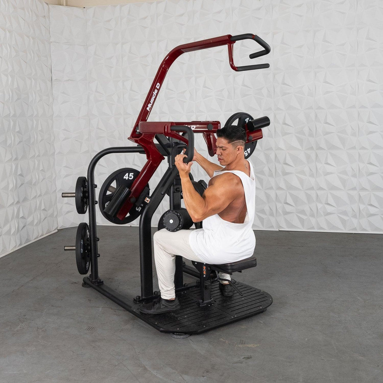 Man in white tank top using a red and black rotary lat pull-down machine with 45lb plates.