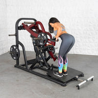 Thumbnail for Woman using a chest-supported plate-loaded row machine with 25lb plates, 45lb plates stored on the side.