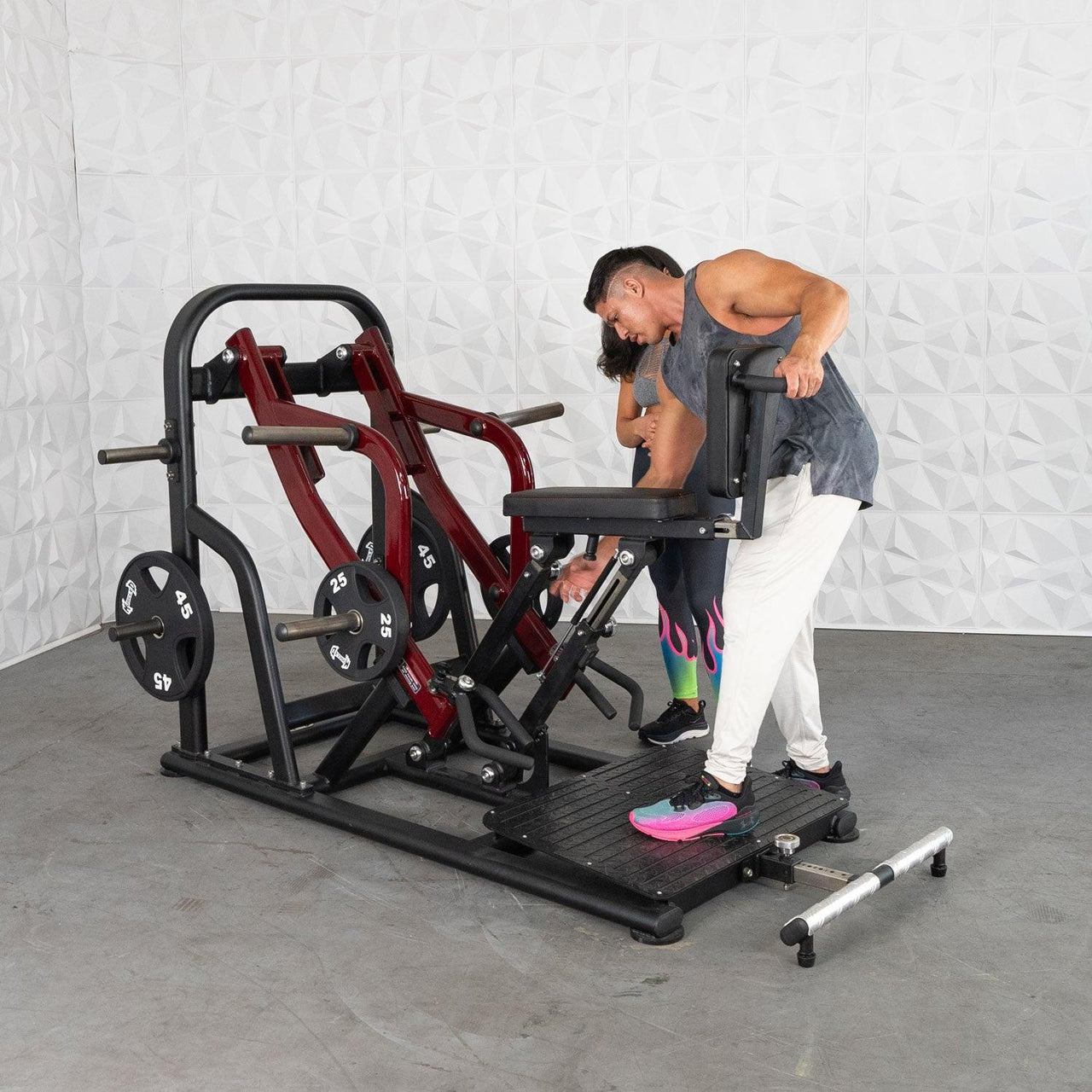 Man and woman adjusting a red and black chest-supported row machine with weight plates.