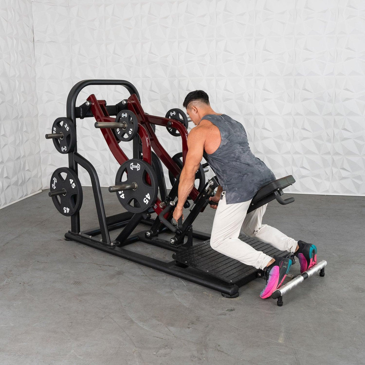 Man using a chest-supported plate-loaded rowing machine with black and red frame and weight plates.