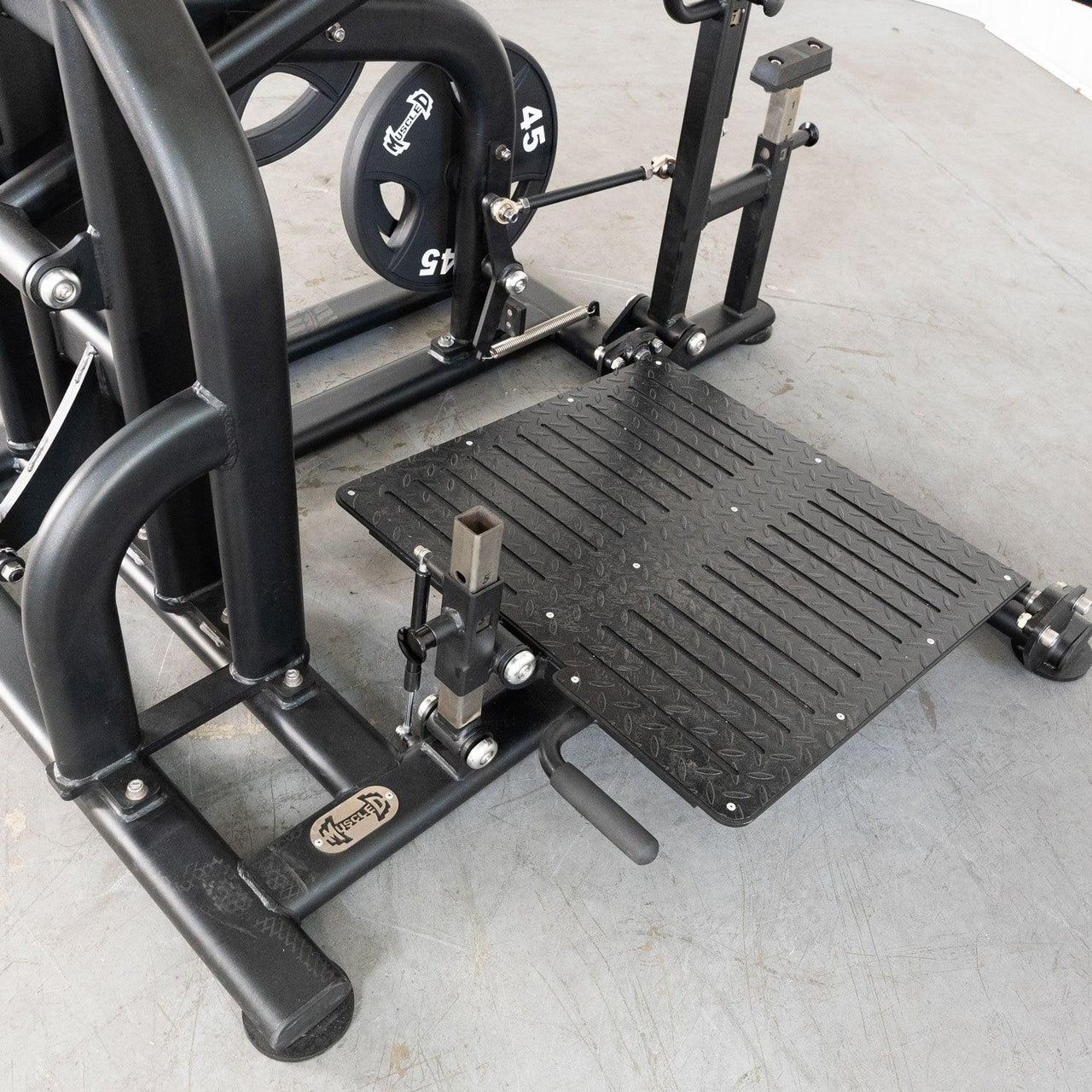 Close-up of a black plate-loaded squat machine with a textured foot platform and 45 lb weight plates.