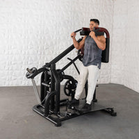 Thumbnail for Man using a black plate-loaded squat machine with red shoulder pads and a textured white wall in the background.