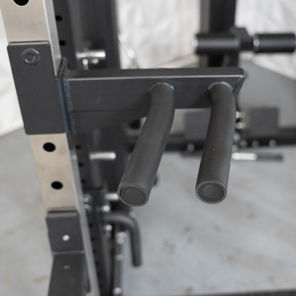 Close-up of black dip handles attached to a silver and black power rack.