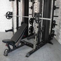 Thumbnail for Black and silver multi-functional fitness machine with an adjustable bench and barbell loaded with 25lb plates.