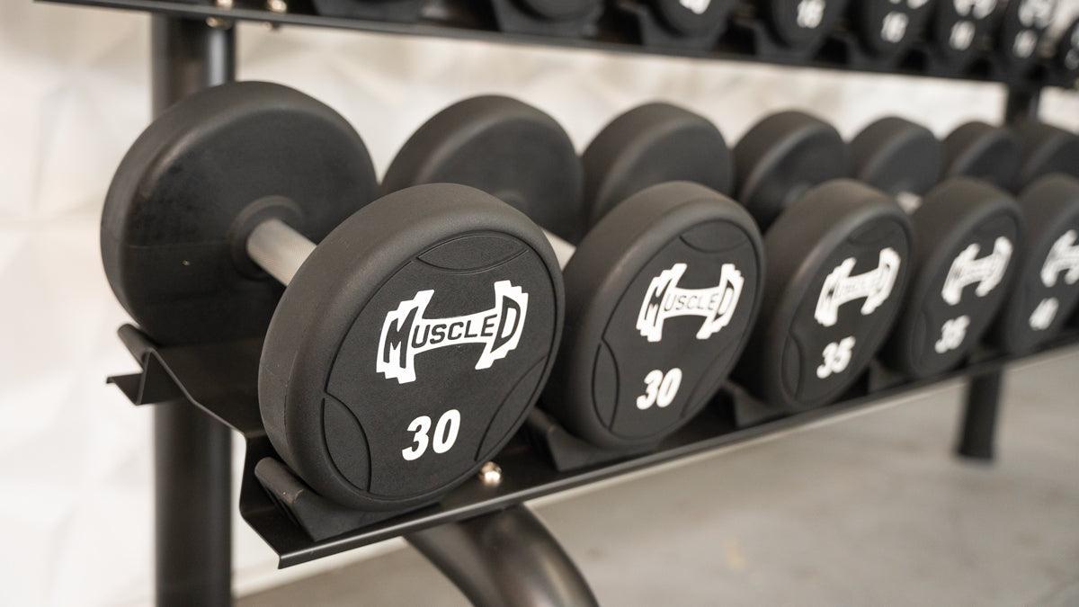 Black urethane dumbbells with "MUSCLE D" logo and weight numbers (30, 35) on a rack.