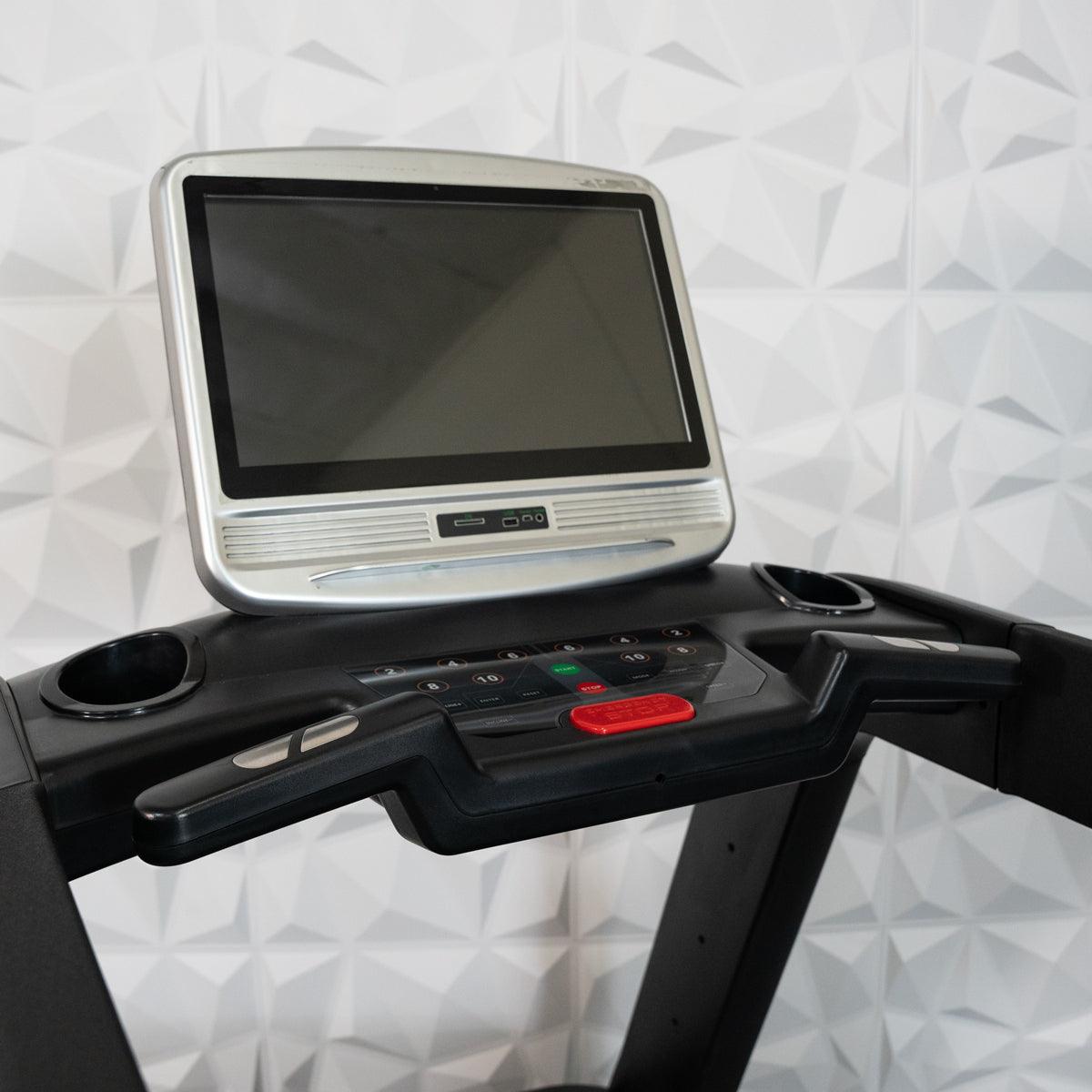 Close-up of a treadmill console with a large, silver-framed touch screen and control buttons.