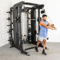 Thumbnail for Man in blue tank top using a black multi-station home gym with weight plates.
