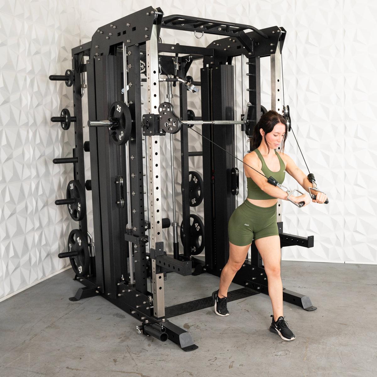 Woman in green activewear using a large black and silver multi-gym machine with cable pulleys.