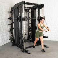 Thumbnail for Woman in green activewear using a large black and silver multi-gym machine with cable pulleys.