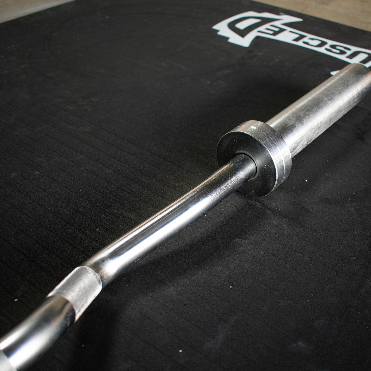 Close-up of a hard chrome curl bar with an ergonomic angle, resting on a black mat with the Muscle D Fitness logo.