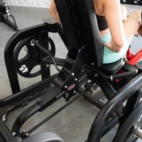 Thumbnail for Person using a black plate-loaded abductor/hip extension machine with 45lb weight plates.
