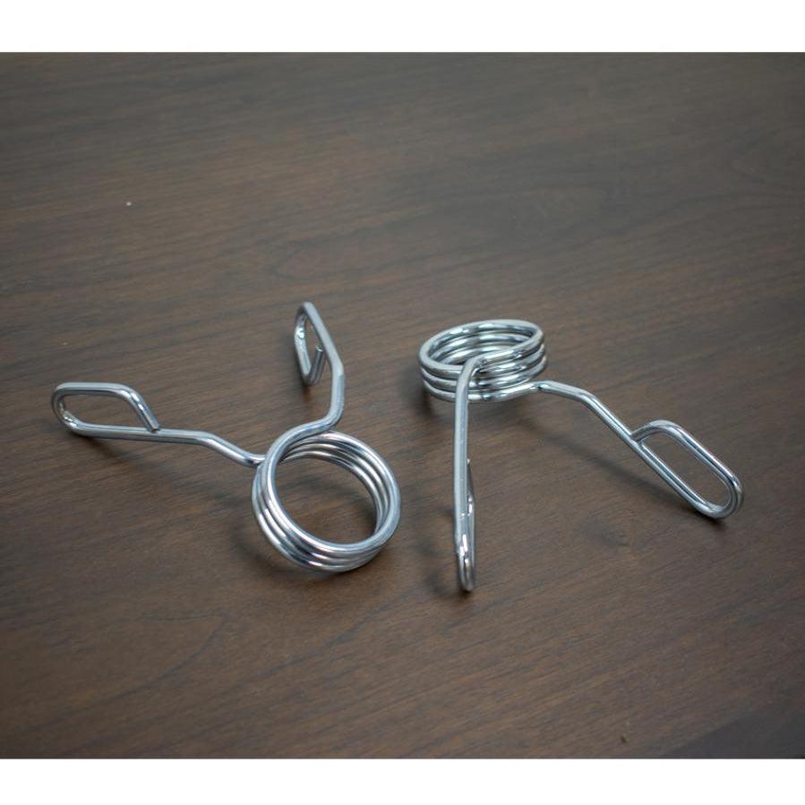 Pair of silver spring collars for barbells on a dark wood surface.