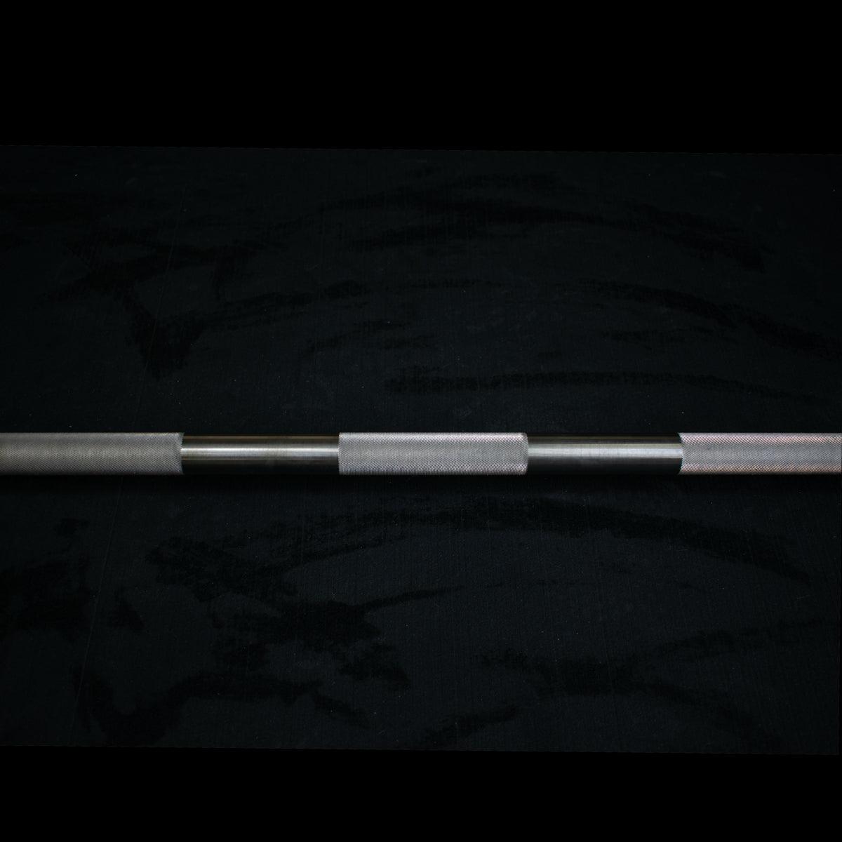 Close-up of a stainless steel Olympic barbell with knurling on a dark background.