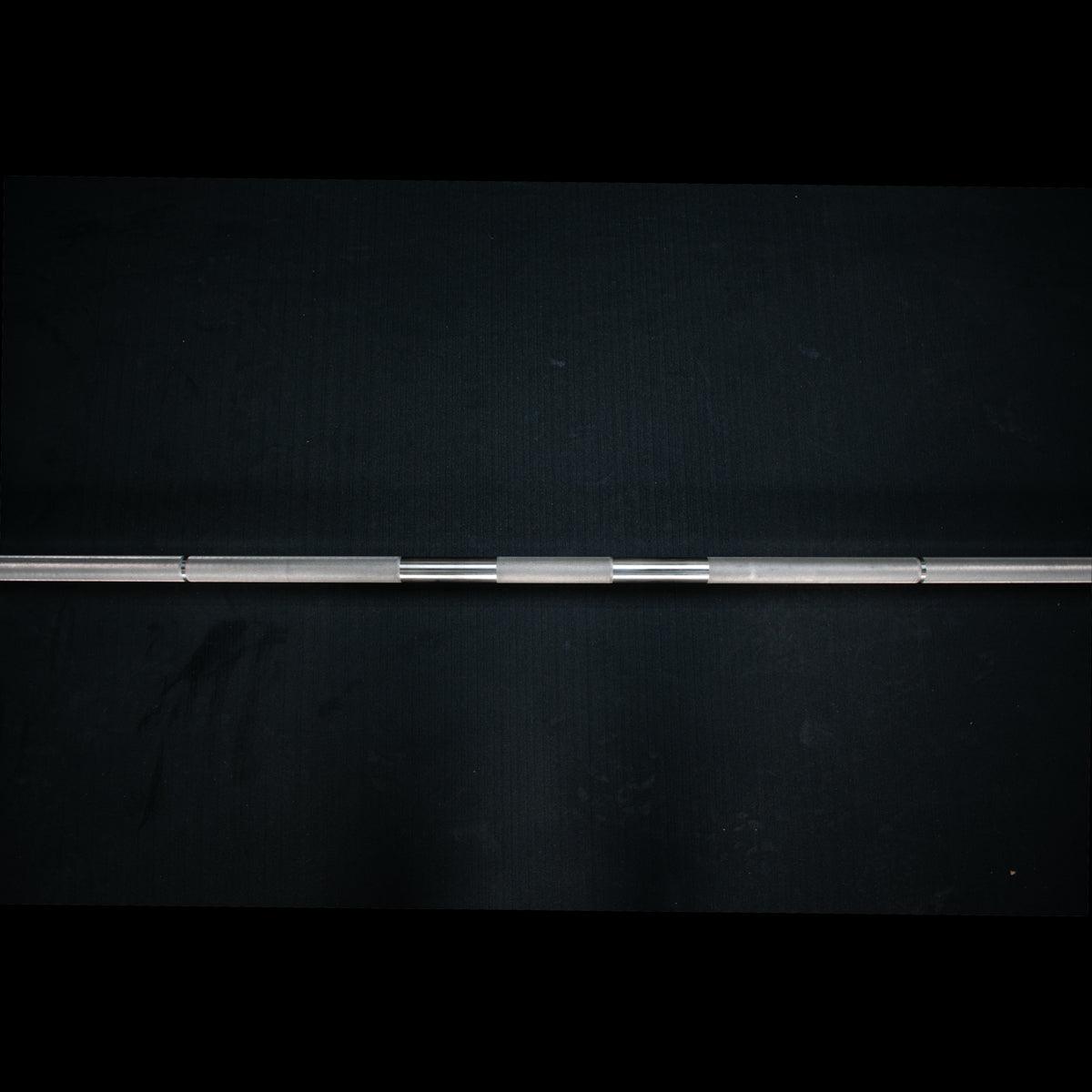 Stainless steel Olympic bar with knurled sections on a dark background.