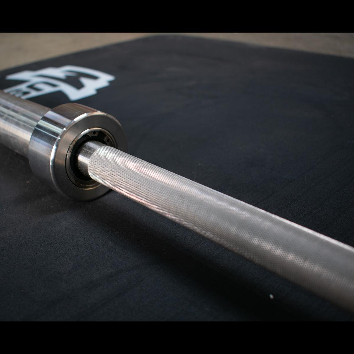 Close-up of a stainless steel Olympic bar with knurling and a bearing sleeve.