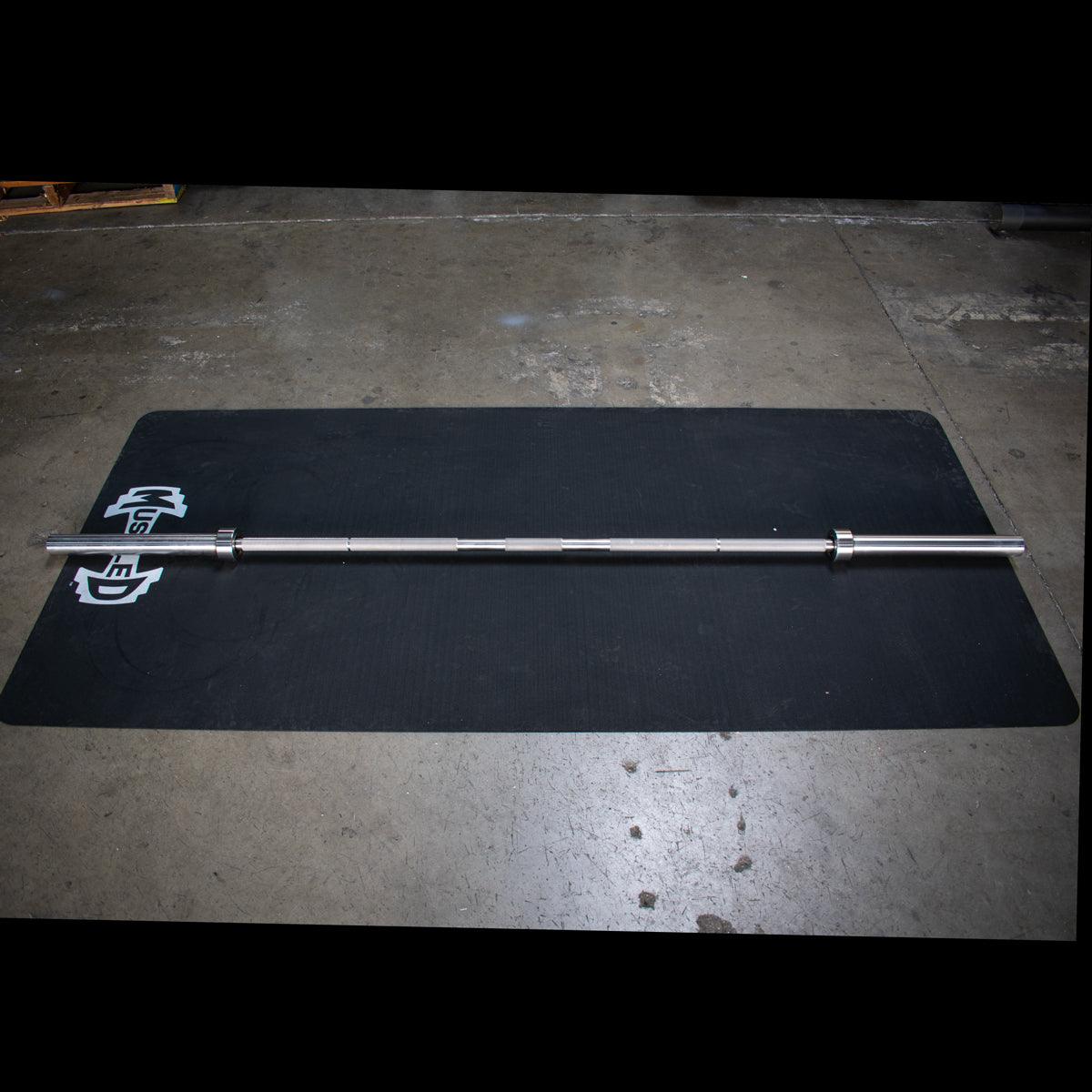 Stainless steel Olympic barbell with knurling on a black mat.