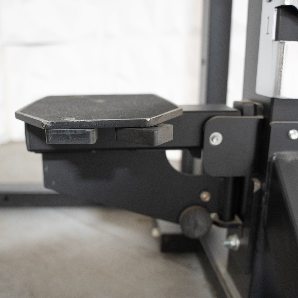 Close-up of a black, hexagonal footplate attached to a fitness rack, with a textured, non-slip surface.