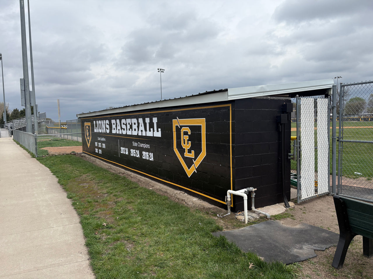 Black dugout wrap with gold Lions Baseball lettering, a CL logo and state champion years on a baseball field