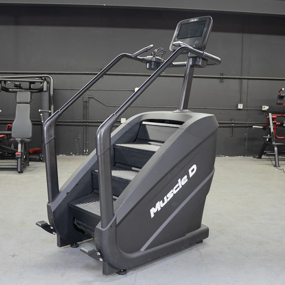 Black Muscle D Fitness stair climber with a touchscreen display and handrails in a gym setting.