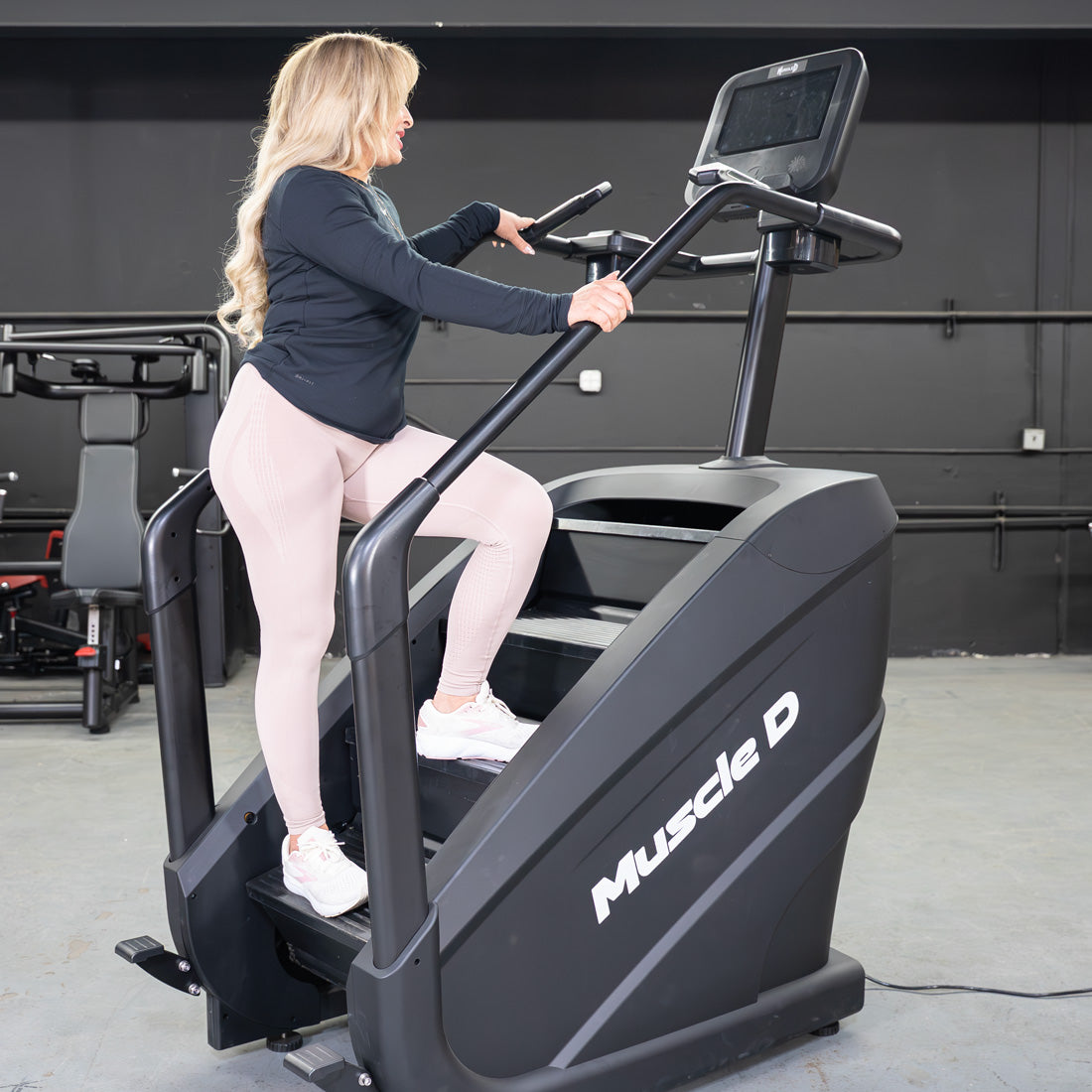 Woman exercising on a black Muscle D Fitness stair climber with a touchscreen display.