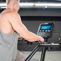 Thumbnail for Man in a gray tank top using a black stair climber with a large touchscreen display.