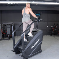 Thumbnail for Man in a gym using a black Muscle D Fitness stair climber with a touchscreen display.