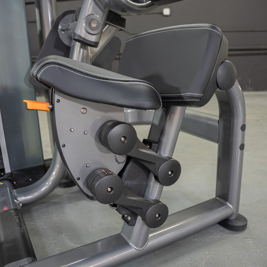 Close-up of the black padded seat and armrests of an ab crunch machine with an orange adjustment lever.