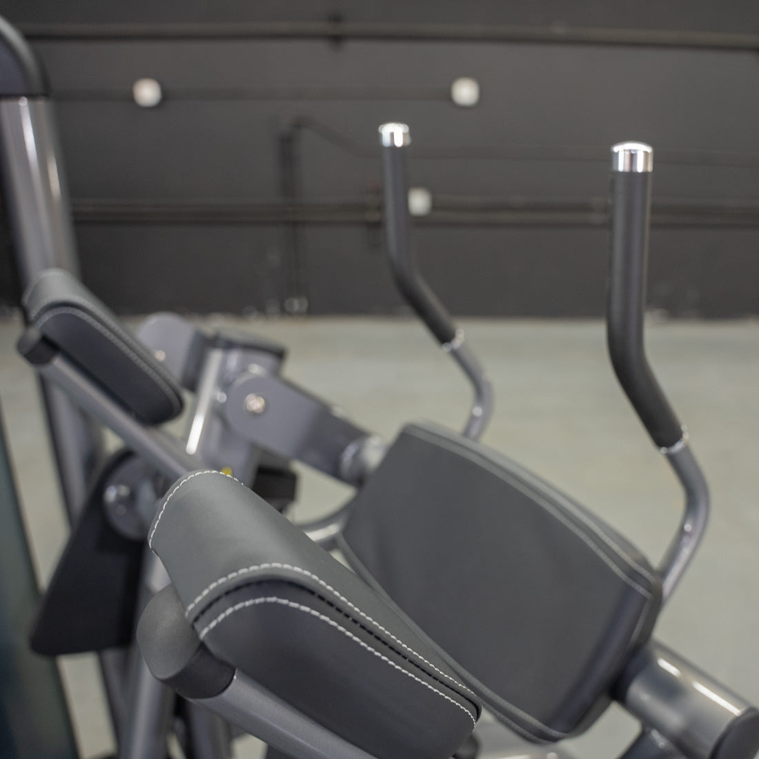 Close-up of a gray ab crunch machine with padded armrests and handles.