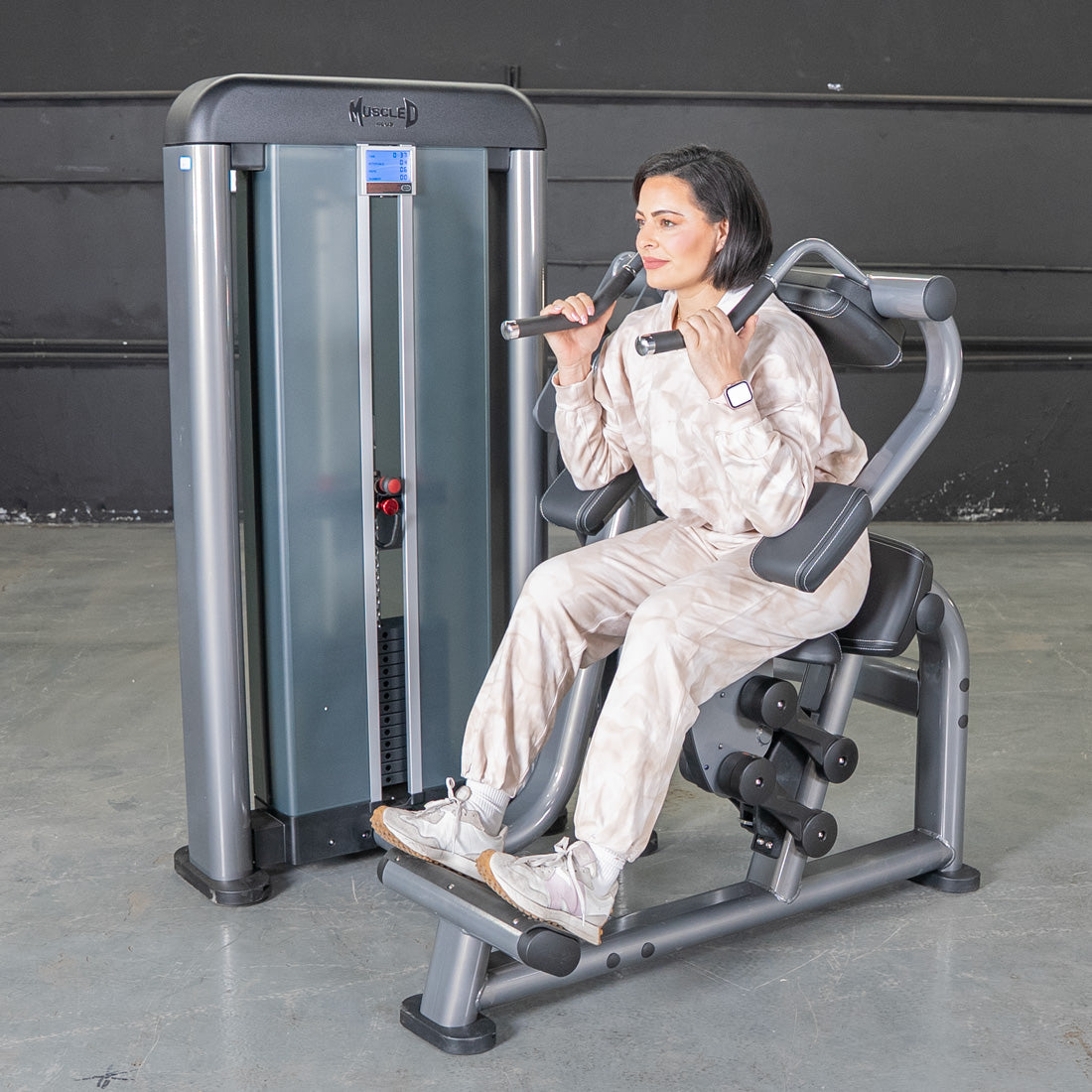 Woman using a gray and black ab crunch machine with a weight stack.