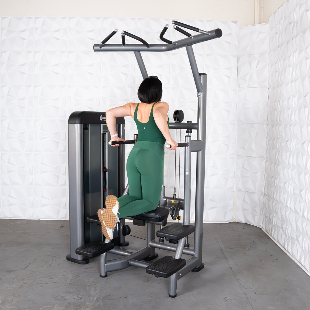 Woman in green performing assisted dips on a commercial-grade chin/dip machine.