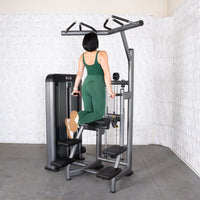 Thumbnail for Woman in green using an assisted chin/dip machine, kneeling on the pad and holding dip handles.