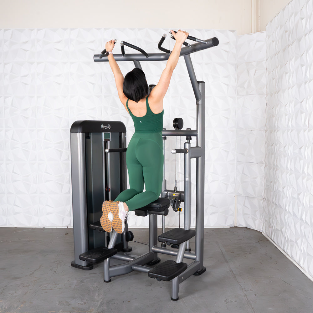 Woman in green performing assisted chin-ups on a gray fitness machine.