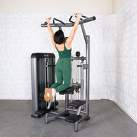 Thumbnail for Woman in green performing assisted chin-ups on a gray fitness machine.