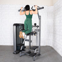 Thumbnail for Woman in green doing an assisted chin-up on a gray commercial-grade fitness machine.