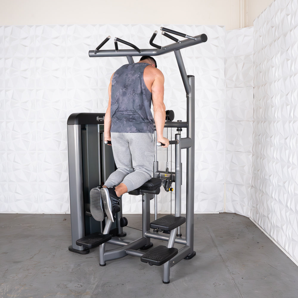 Man using an assisted chin/dip machine, facing away, with his knees on the padded support.