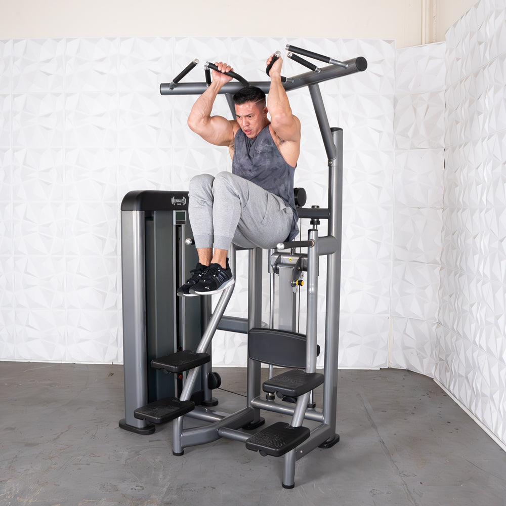 Man using a gray assisted chin/dip machine, holding handles and lifting his knees.