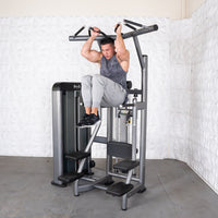 Thumbnail for Man using a gray assisted chin/dip machine, holding handles and lifting his knees.