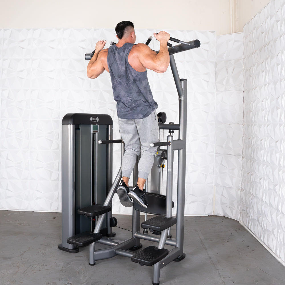Man doing assisted pull-ups on a gray commercial-grade chin/dip machine with adjustable seat and pin selectorized weights.