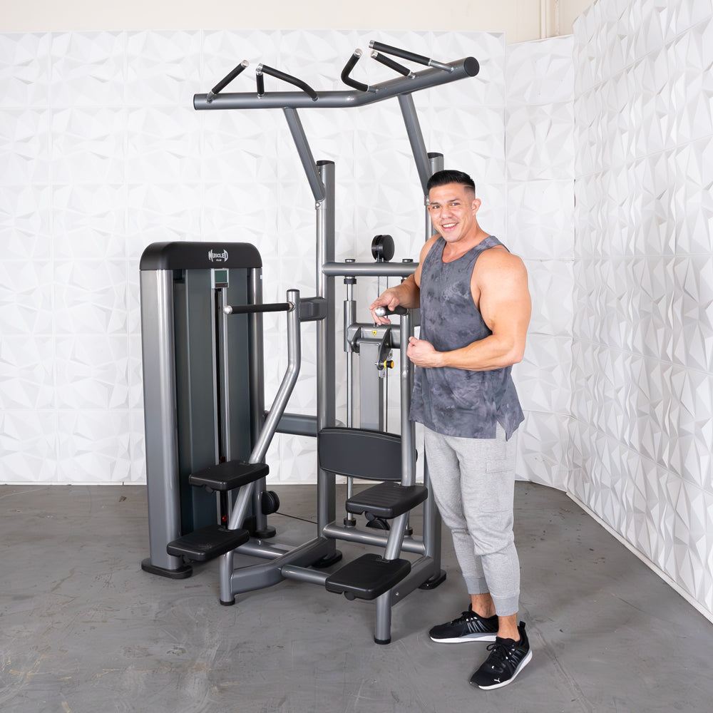 Man standing next to a gray assisted chin/dip machine with an adjustable seat and pin selectorized weight stack.